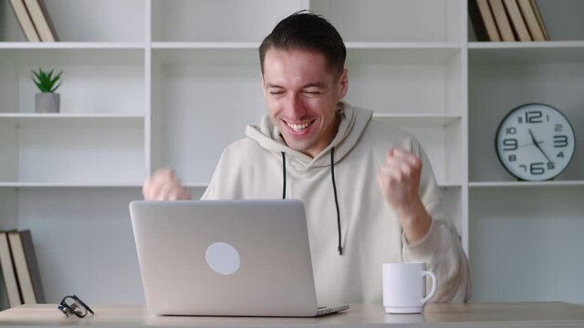 Overjoyed business man sit at desk look at laptop screen, scream celebrating success win at modern office. Excited male guy hipster feel euphoric receiving pleasant email message on computer