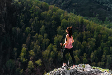 Naklejka premium Hiking in the mountains. A woman is engaged in Nordic walking in the mountains. Tourist in the mountains. A young woman engaged a nordic walking in a mountains. Active leisure time concept. Copy space