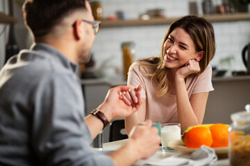 Beautiful young girl enjoying in breakfast with her boyfriend. Loving couple drinking coffee in the kitchen.