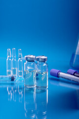 Glass ampoules with liquid for injection against laboratory flasks on dark background. Vaccination from coronavirus Covid-19 theme