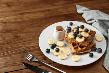 Oatmeal Belgian waffles topped with banana and blueberry on rustic wooden table
