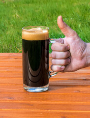 a cup of dark beer on a orange table on a natural green background, pinta of black stout close up, glass of ale