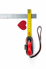 A red cardboard heart is measured with a ruler and a tape measure on a white background.