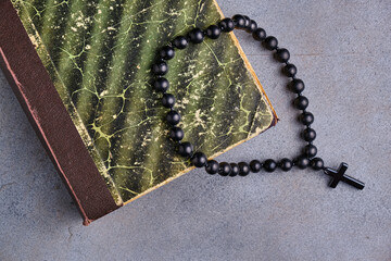Fragment of an old worn book and a black obsidian rosary with a cross on an abstract gray...