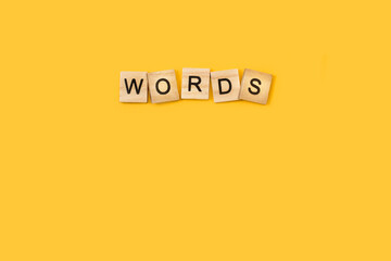 Words escrita con cubos de madera sobre un fondo amarillo liso y aislado. Vista superior. Copy space