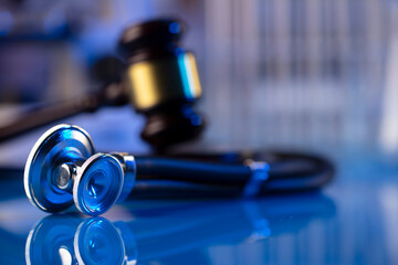 Medical law concept. Gavel and stethoscope on the glass table. Blue light.