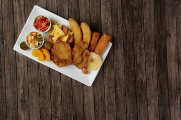 Cuban filet. Made with Breaded Steak, Banana, Breaded Cheese and Ham, French Fries with Bacon. Vinaigrette, vegetables, and fruits. Served on the porcelain platter. Top view with free space for text.