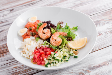 Salad with shrimps, tomatoes, avocado, egg, cucumber on a white plate on a light wooden background. Photo for the menu and site. Space for text