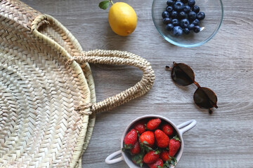 Straw bag, sunglasses and various fruit on wooden background. Flat lay.