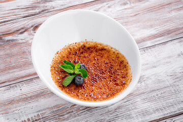 Creme brulee with sugar crust on a white plate on wooden background. close up. Macro photo
