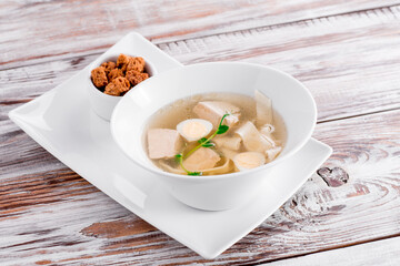 Transparent beef broth with egg, garnished with dill in a white bowl on a wooden background. Photo for the menu. Close up