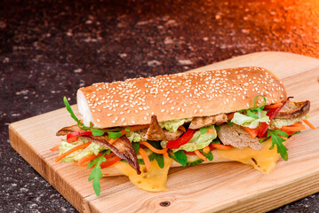 Fresh baguette sandwiches with veal, sliced cheese, tomatoes and fresh lettuce on wooden cutting board. Dark red background. Top view. Space for text