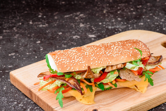 Fresh baguette sandwiches with veal, sliced cheese, tomatoes and fresh lettuce on wooden cutting board. Dark black background. Top view. Space for text