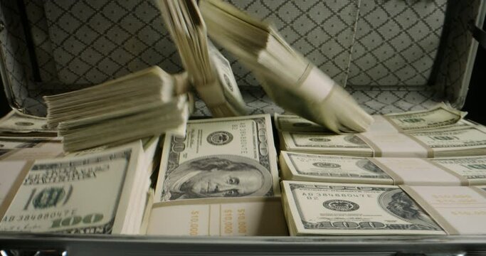 Packs of cash falling into a metal case filled with money. 100 dollar bills in a briefcase that gets closed. Finance, investing, business concept close up 4k footage