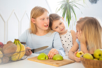 Fototapeta premium Children in the kitchen have fun and eat apples, kids cook breakfast together, cut an apple with a knife in a bright interior