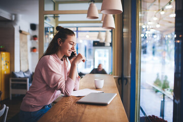 Fototapeta premium Cheerful freelancer speaking on smartphone in cafeteria