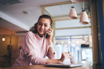 Fototapeta premium Cheerful woman speaking on smartphone in cafeteria