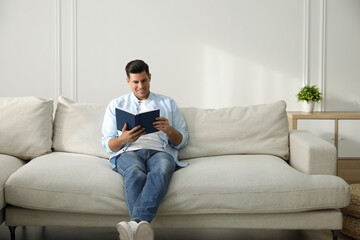 Obraz premium Man with book sitting on comfortable sofa in living room