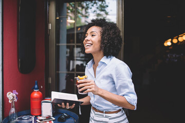 Pleased woman with cocktail and opened notebook standing outside