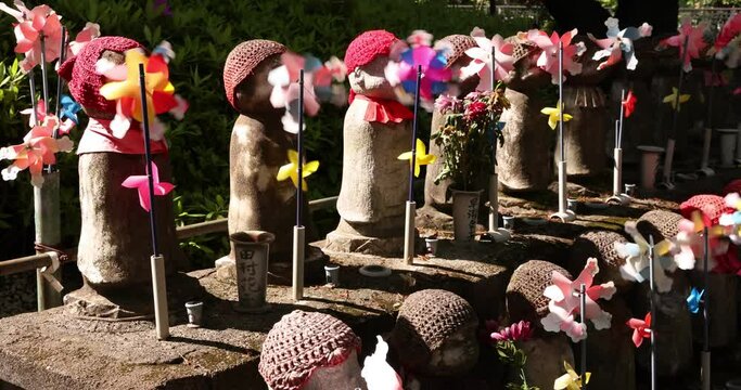 A slow motion of moving colorful windmills with Jizo statue daytime