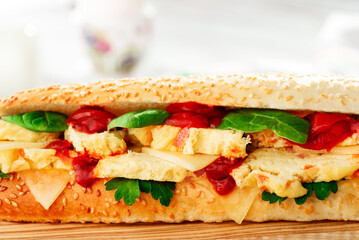 Fresh baguette sandwiches with omelette, basil, tomato sauce and fresh salad on a wooden cutting board on a light wooden background. Space for text