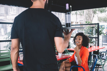 Waiter with bottle of wine providing service to female visitor in cafe