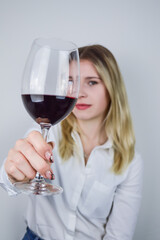 Portrait of a beautiful young blonde woman who raises a glass of red wine to appreciate its color and nuances at a wine tasting - Focus on the glass of wine