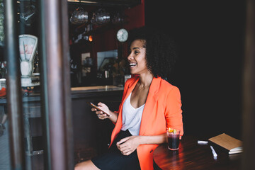 Smiling black female woman with smartphone and drink in cafe