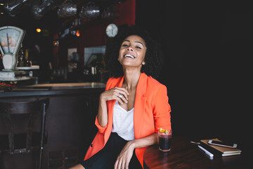 Fototapeta na wymiar Happy black woman with glass of cocktail in cozy bar