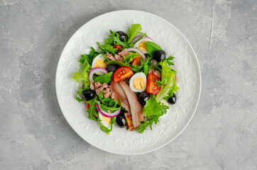 French salad Nicoise with tuna, egg, green beans, tomatoes, olives, lettuce, onions and anchovies on a gray concrete background. Healthy food.
