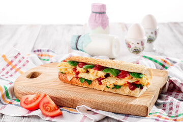 Fresh baguette sandwiches with omelette, basil, tomato sauce and fresh salad on a wooden cutting board on a light wooden background. Space for text