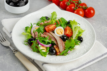 French salad Nicoise with tuna, egg, green beans, tomatoes, olives, lettuce, onions and anchovies on a gray concrete background. Healthy food.