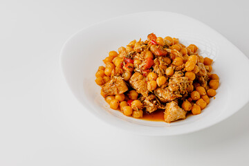Stewed chickpeas with chicken and vegetables and herbs on white plate. White background. Copy space.