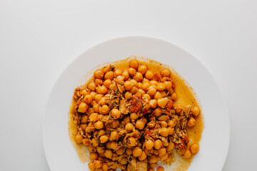 Stewed chickpeas with chicken and vegetables and herbs on white plate. White background. Copy space.