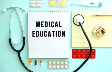 A notebook with the text MEDICAL EDUCATION is neatly folded among the pills, a stethoscope, and a...