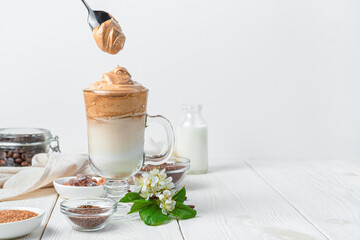 Dalgona iced coffee and foam spoon on a white background with ingredients and colors.