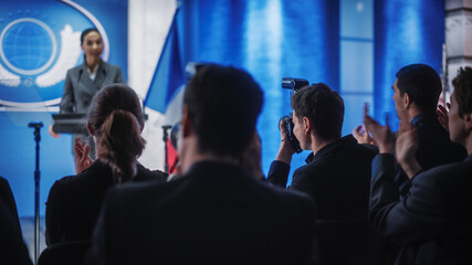 Fototapeta premium Pool of Photographers and Journalists Working at a Organization Press Conference with Female Representative Delivering a Speech at Press Conference in Government Building. Diplomat at a Summit.