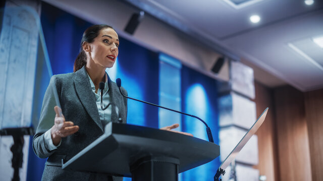 Portrait Of Organization Female Representative Speaking At Press Conference In Government Building. Press Office Representative Delivering A Speech At Summit. Minister Speaking To Congress Hearing.