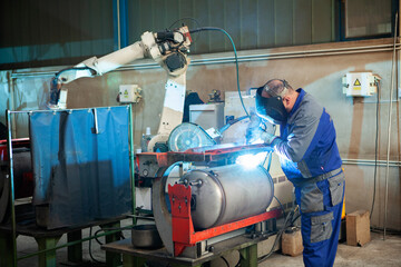 Man and machine welding together, worker and robotic arm welding boiler with argon gas