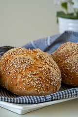 Fresh challah bread rolls hot from the oven wrapped in a towel. Gluten free bread buns or mini loaves with sesame seeds and golden color ready to eat. Fluffy homemade bread, with flowers in background