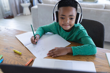 African american boy in online school class, using headphones and laptop