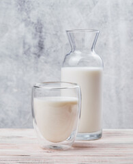 Vegan milk in transparent glass and Milk bottle on light concrete background. Space for text