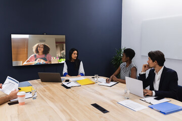 Diverse group of business colleagues having video call with businesswoman on screen in meeting room