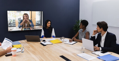 Diverse group of business colleagues having video call with businesswoman on screen in meeting room