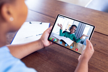 Caucasian female teacher sitting at desk using smartphone having online lesson with pupil