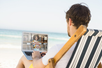 Caucasian man relaxing on beach having video call using laptop