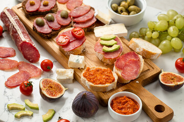 Assortment of sausages and cheese, salami, grapes, baguette slices, olives, on white background. Close up