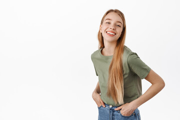 Obraz premium Carefree authentic girl with white perfect smile, happy emotions, holding hands in jeans and looking cheerful at camera, standing against white background
