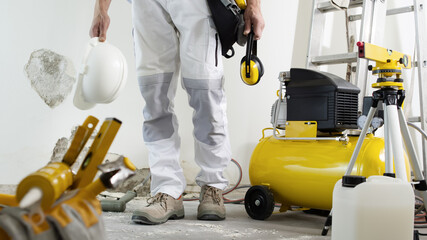 house renovation concept, construction worker holds in hands helmet and safety headphones, air...