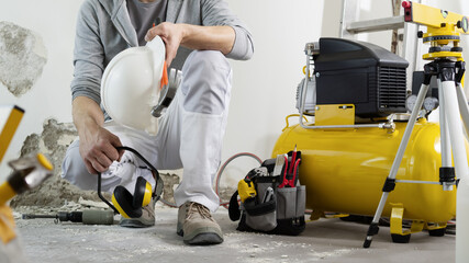 house renovation concept, construction worker holds in hands helmet and safety headphones, air...